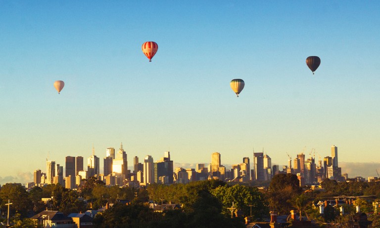 Image shows hot air balloons floating over the Melbourne city skyline.